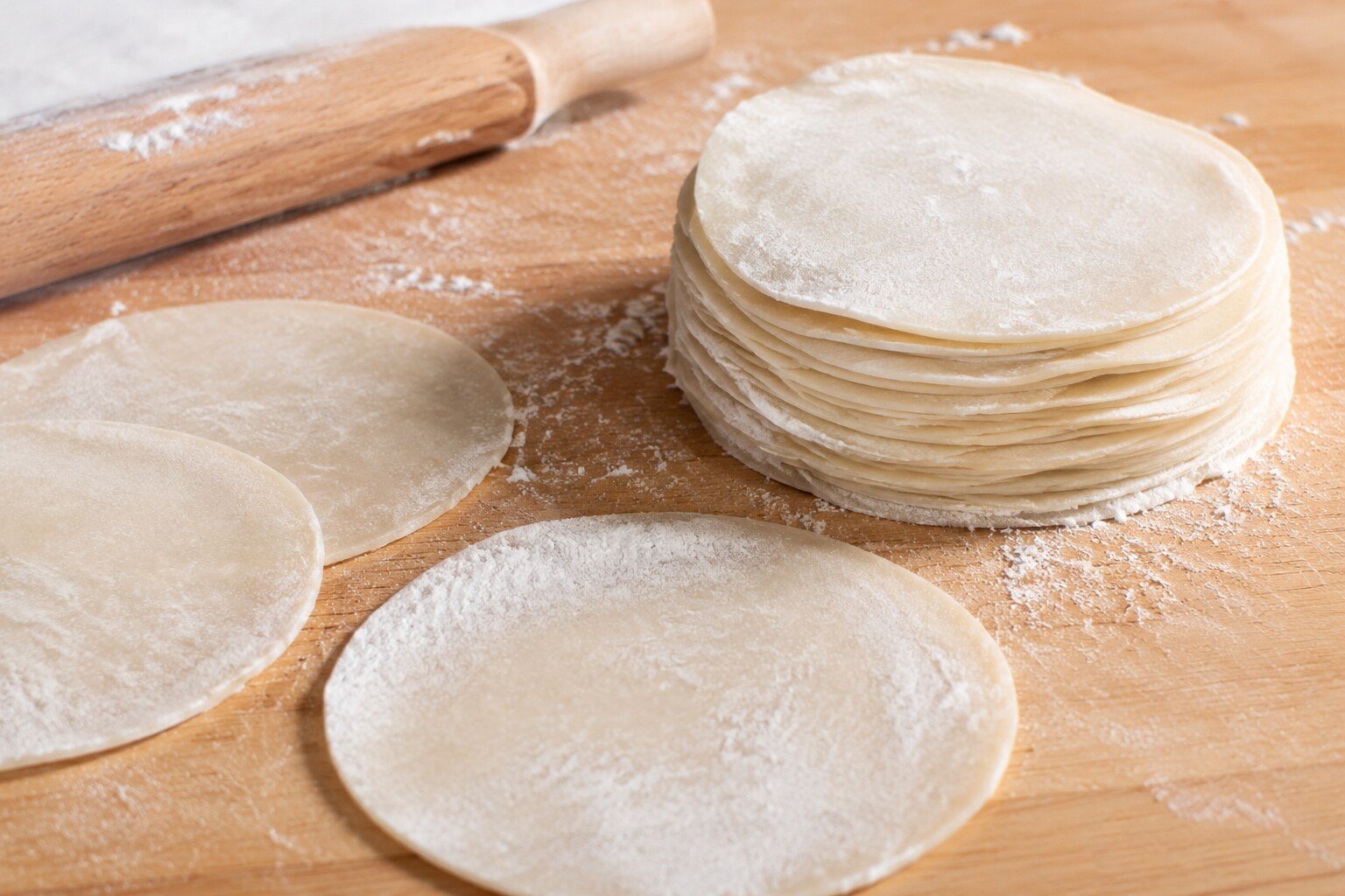 Thin round homemade dumpling wrappers on a wooden board with a rolling pin